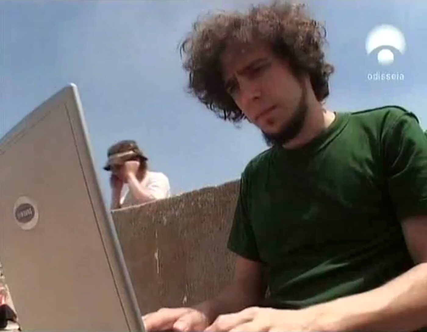 A person working on a laptop outdoors against a bright sky.